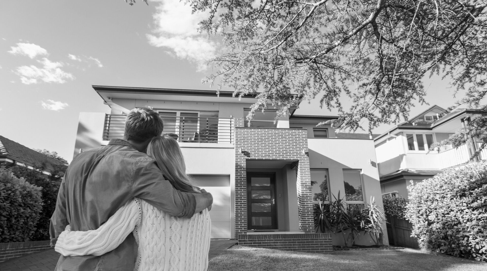 Ein glückliches Paar steht vor einem modernem Haus und hält sich in den Armen